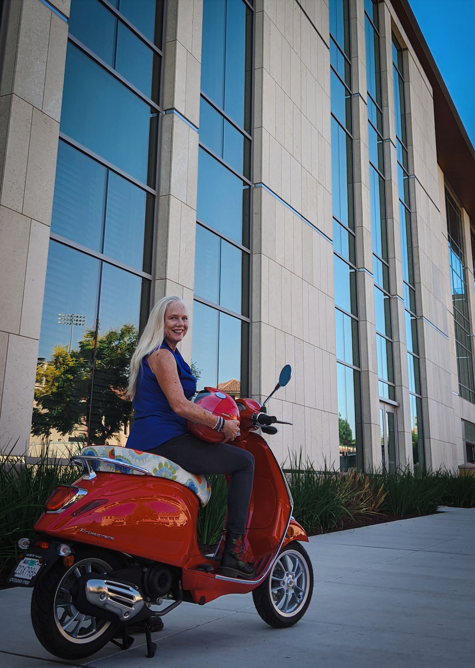 Executive Director Brigit Helms sits on her red Vespa.